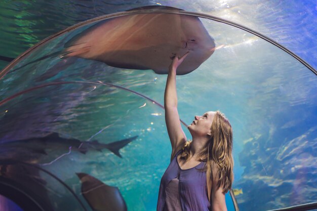 Een jonge vrouw raakt een pijlstaartrogvis aan in een oceanariumtunnel.