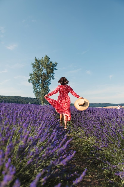 Een jonge vrouw rent in een lavendelveld en houdt een strohoed vast