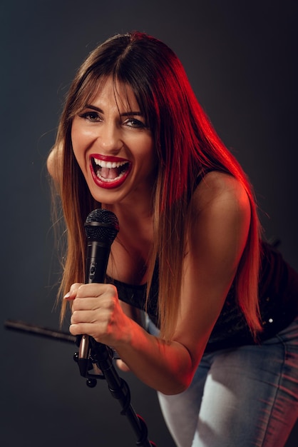 Een jonge vrouw rockzanger met een microfoon met standaard en zingen met een wijd open mond. Camera kijken.