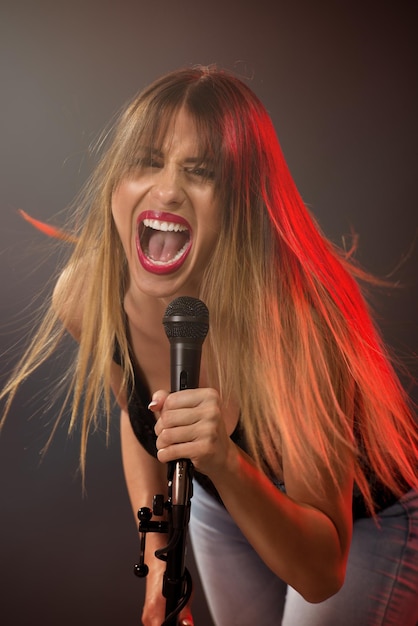 Een jonge vrouw rockzanger met warrige lange haren met een microfoon met standaard en zingen met een wijd open mond.