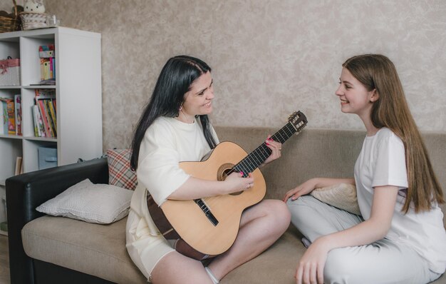 Een jonge vrouw speelt gitaar voor haar dochter. Ze zitten op de bank in hun appartement.