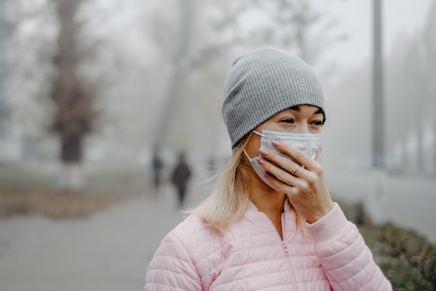 Een jonge vrouw staat in de herfst in de buurt van de weg met een medisch masker.