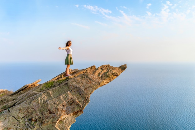 Een jonge vrouw staat op een schilderachtige steile klif boven de zee tegen de lucht