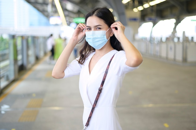 Een jonge vrouw staat op het metroplatform en draagt een gezichtsmasker, Covid-19-bescherming, Nieuw normaal reisconcept.