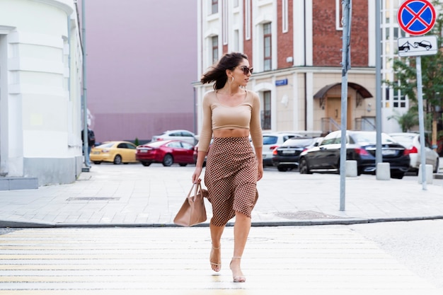Een jonge vrouw steekt de weg over in de stad. Mooie stijlvolle brunette met een tas.