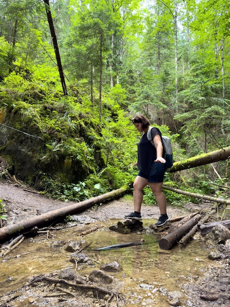 Een jonge vrouw steekt een kleine rivier over op rotsen in het bos.