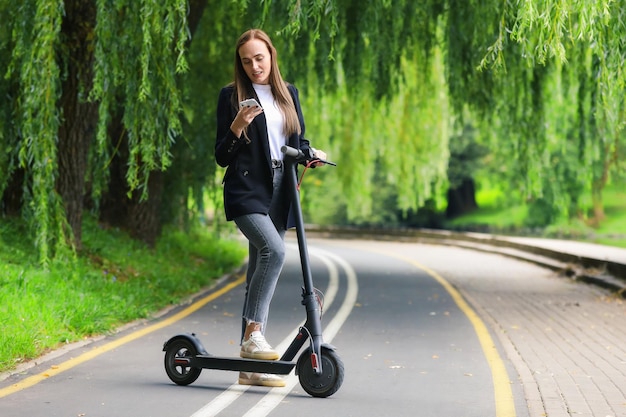 Een jonge vrouw typt op haar telefoon terwijl ze op een scooter rijdt hipster op eco-transport