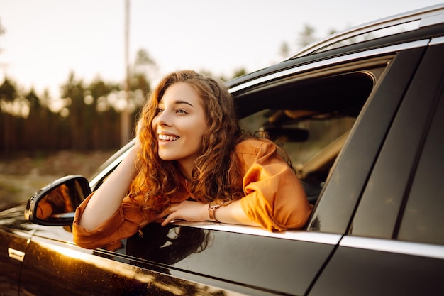 Een jonge vrouw voelt vrijheid uit een auto raam leunend in een zonnig bos Reizen concept
