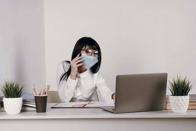 Een jonge vrouw werkt op afstand op kantoor met een beschermend masker tijdens een epidemie