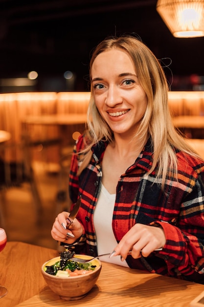 Een jonge vrouw zit aan een tafel en houdt een vork en een mes vast in een restaurant