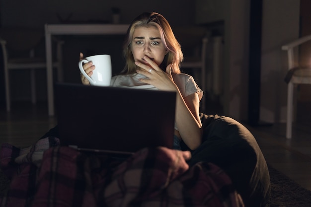 Een jonge vrouw zit alleen thuis en kijkt naar een horrorfilm