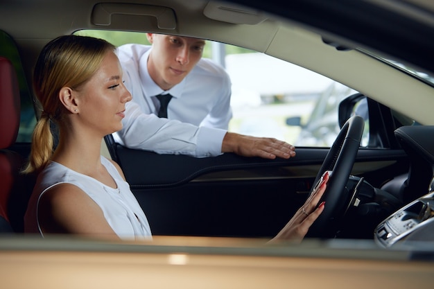 Een jonge vrouw zit in een auto terwijl een verkoopagent over een nieuwe auto praat