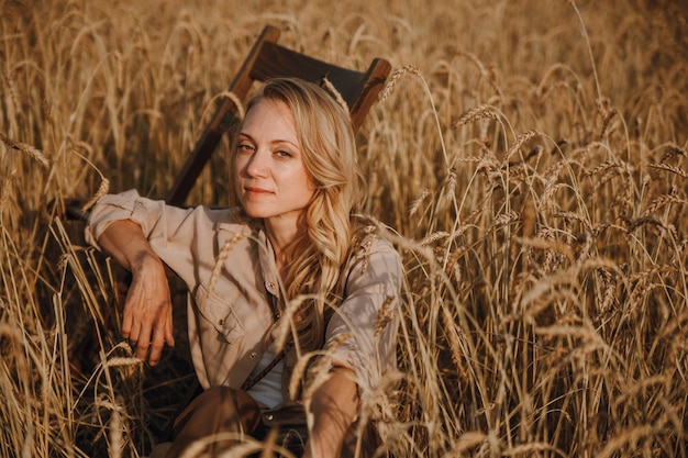 Een jonge vrouw zit in een tarweveld glimlachend en geniet van de zonsondergang