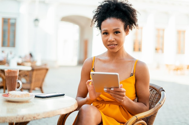 Een jonge vrouw zit in een zomerrestaurant Hij eet ontbijt in een café en werkt op een tablet