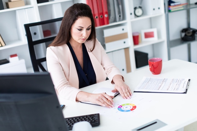 Een jonge vrouw zit op een computer Bureau, houdt een pen en werkt met een grafiek en een computer.