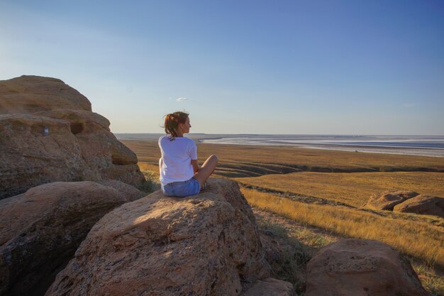 Een jonge vrouw zit op een grote steen en kijkt in de verte op de steppe aan het meer