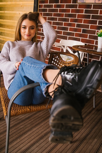 Foto een jonge vrouw zit op een stoel. het meisje tilde speels haar voeten op de stoel. vreugde en een glimlach op het gezicht van het meisje.