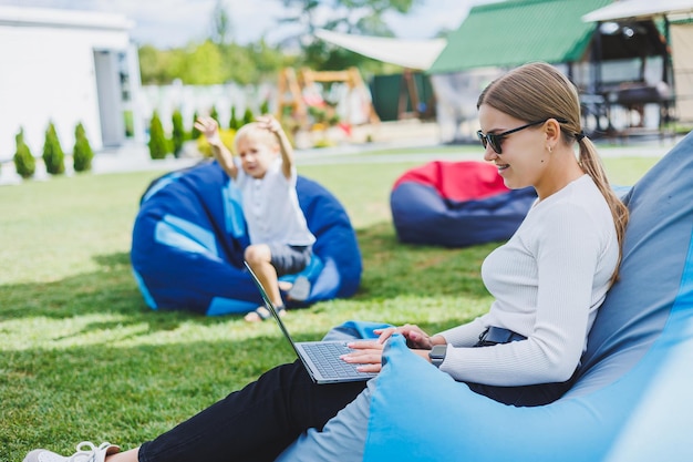 Een jonge vrouw zit op een zachte stoel in het park en werkt op een laptop Buitenshuis werken