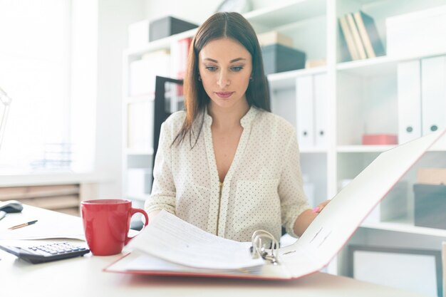 Een jonge vrouw zit op kantoor op een computer Bureau en bladeren door een map met documenten.