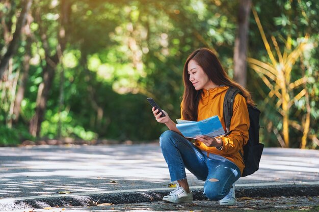 Een jonge vrouwelijke backpacker op zoek naar richting op mobiele telefoon en een kaart tijdens het reizen op een bergweg