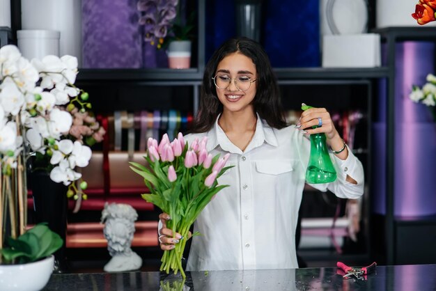 Een jonge vrouwelijke bloemist zorgt voor bloemen in een gezellige bloemenwinkel en verzamelt boeketten bloemisten en het maken van emmers in een bloemenwinkel klein bedrijf