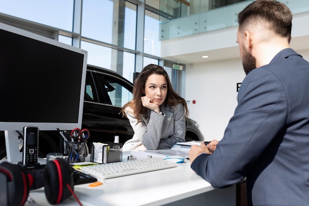 Een jonge vrouwelijke koper in een autodealer leert van een adviseur de details van een transactie voor: