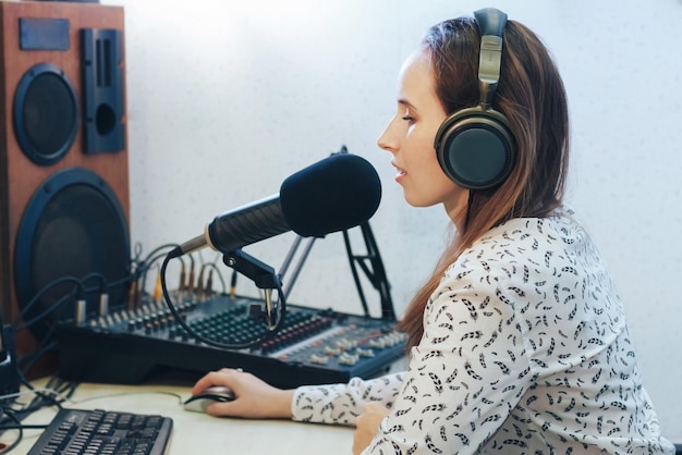 Een jonge vrouwelijke radiopresentator met koptelefoon voor een microfoon en monitor neemt een radioprogramma op in de Studio