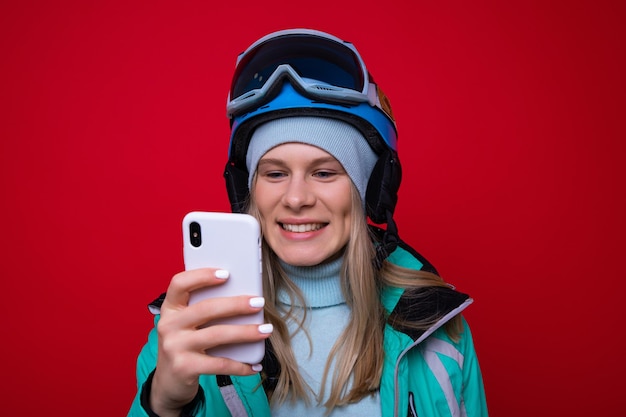 Een jonge vrouwelijke snowboarder typt op haar telefoon op een rode achtergrond