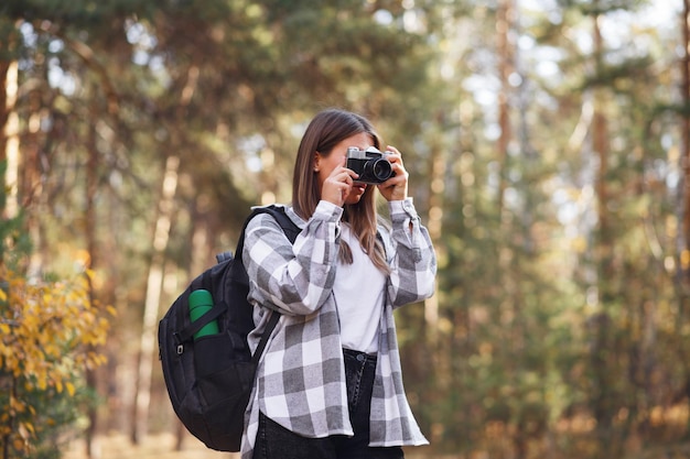 Een jonge vrouwelijke toerist loopt in het bos met een camera en een rugzak op haar schouders