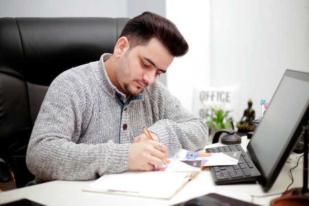 Een jonge werknemer houdt een pen in de hand en schrijft iets op papier.