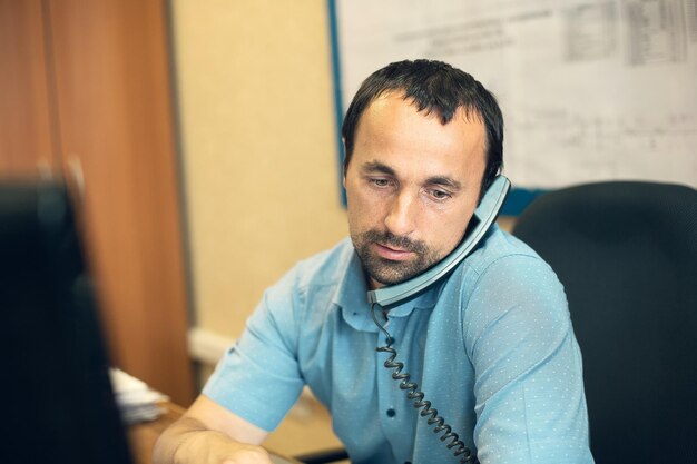 Een jonge werknemer zit in een stoel aan een bureau op kantoor en praat via een bekabelde telefoon