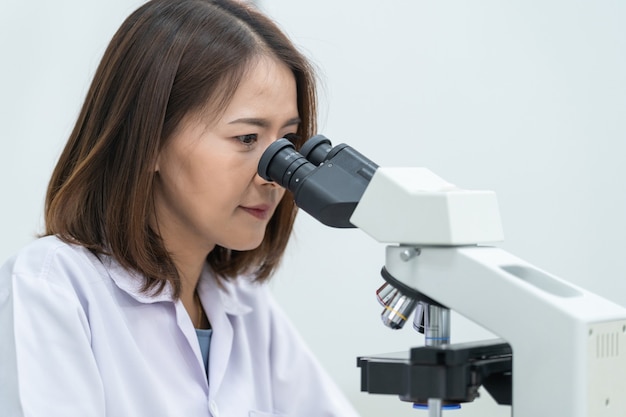 Een jonge wetenschappervrouw in een laboratoriumjas die door een microscoop in een laboratorium kijkt om onderzoek te doen en te experimenteren. Wetenschapper die in een laboratorium werkt. Onderwijs stockfoto's