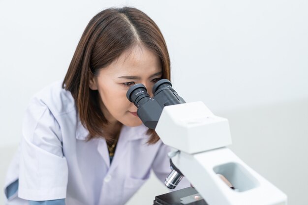 Een jonge wetenschappervrouw in een laboratoriumjas die door een microscoop in een laboratorium kijkt om onderzoek te doen en te experimenteren. Wetenschapper die in een laboratorium werkt. Onderwijs stockfoto's