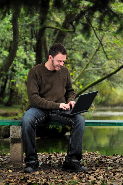 een jonge zakenman die op laptop buiten werkt met groene natuur op de achtergrond