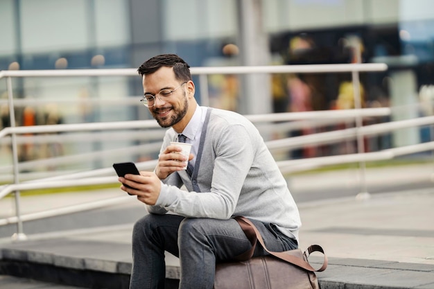 Een jonge zakenman in smart casual zit op de trap in de stad en gebruikt de telefoon