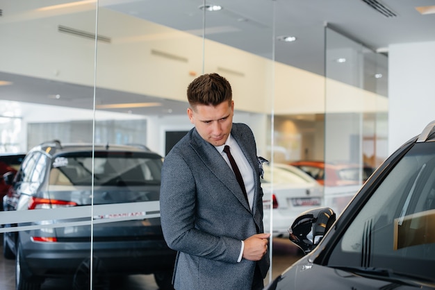 Een jonge zakenman kijkt naar een nieuwe auto in een autodealer. Een auto kopen.