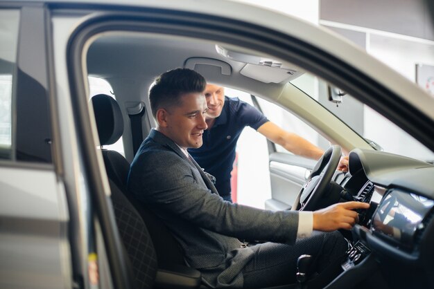 Een jonge zakenman met een verkoper kijkt naar een nieuwe auto in een autodealer. Een auto kopen.