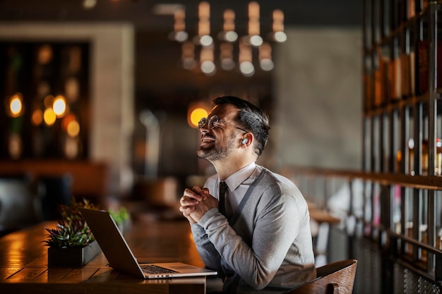 Een jonge zakenman zit in een coffeeshop met zijn laptop en bidt voor succes