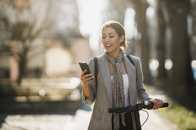 Een jonge zakenvrouw rijdt op een elektrische scooter en gebruikt een smartphone op weg naar haar werk door de stad.