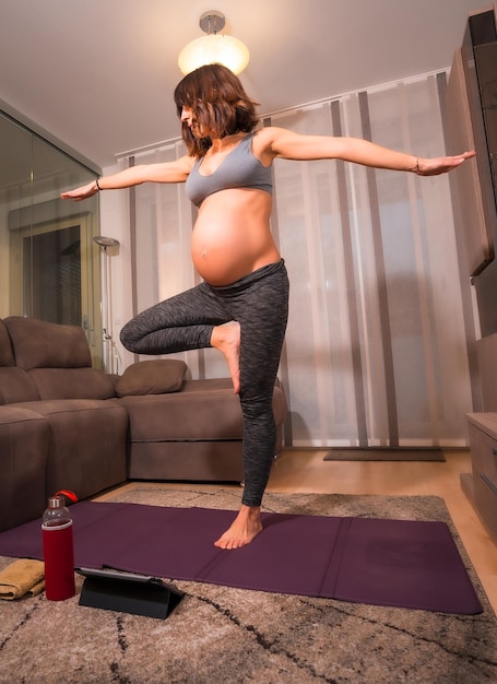 Een jonge zwangere blanke vrouw die pilates doet thuis in de woonkamer Online oefeningen in prepartum lessen