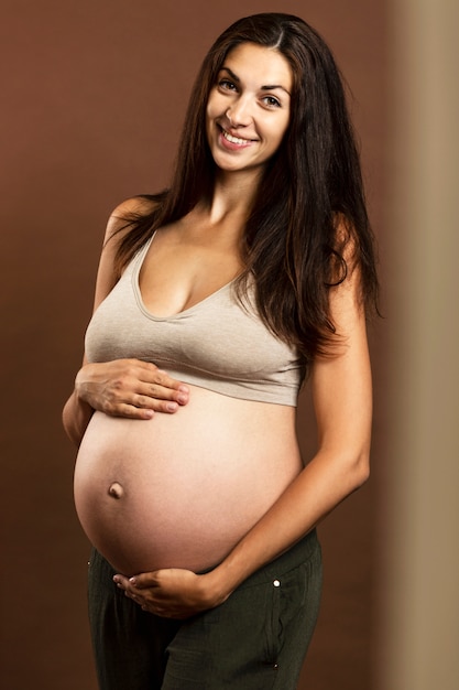 Een jonge zwangere brunette vrouw glimlacht en raakt zacht een grote buik aan. Tederheid en verwachting van geboorte.