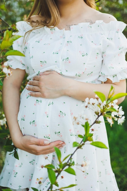 Een jonge zwangere vrouw in een witte jurk loopt in een bloeiende appelboomgaard Gelukkige zwangere vrouw Gelukkige toekomstige moeder