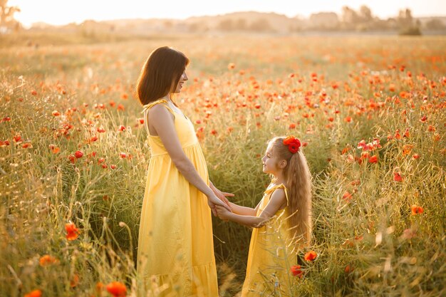 Een jonge zwangere vrouw met haar dochter in gele jurken staat in een papaverveld Familierelaties