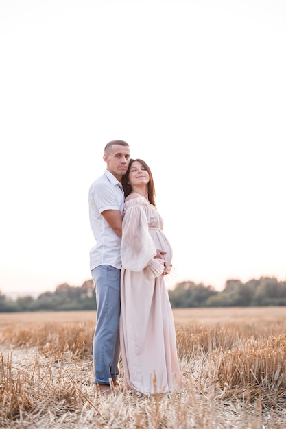 Een jonge zwangere vrouw met haar man een gelukkig mooi paar knuffelen op een gouden veld op het platteland Familierelaties Toekomstige ouders