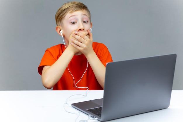 Een jongen achter een laptop in een oranje t-shirt hield zijn handen voor zijn mond en was verrast