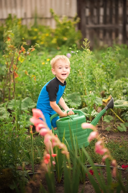 Een jongen die bloemen en een moestuin met een gieter water geeft.