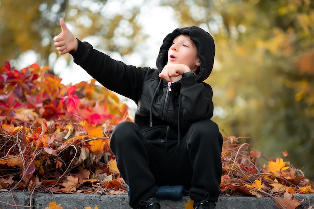 Een jongen die in een prachtig herfstpark zit, wijst met zijn hand naar de kant.