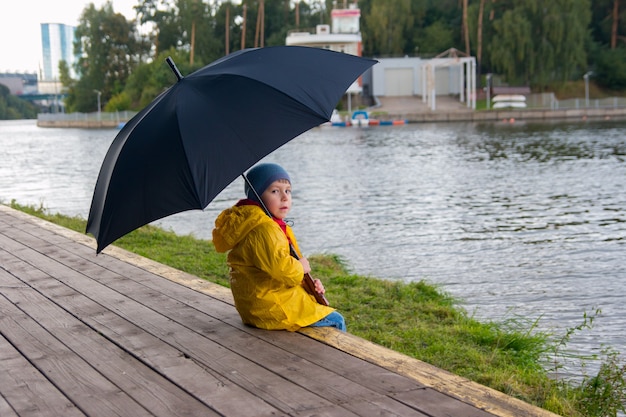Een jongen die onder een paraplu loopt in een gele regenjas. bewolkt weer