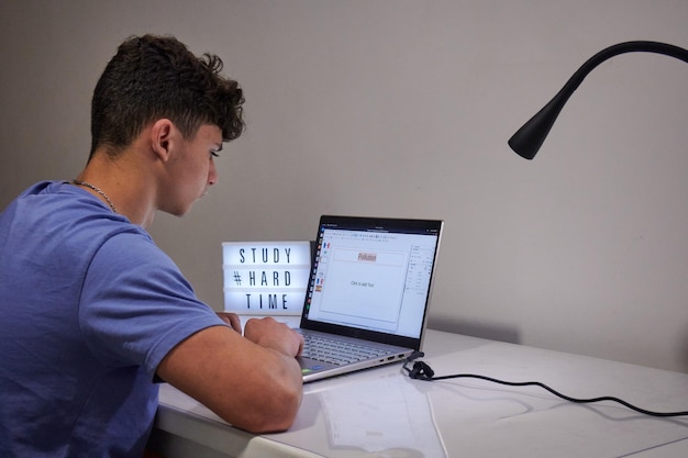 Een jongen die op de laptop werkt met een lamp en een bureau met tekst studeert harde tijd