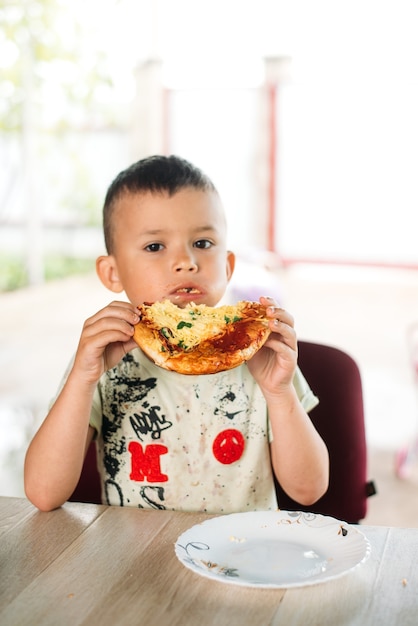 Een jongen, een kind op straat eet een minipizza erg smakelijk